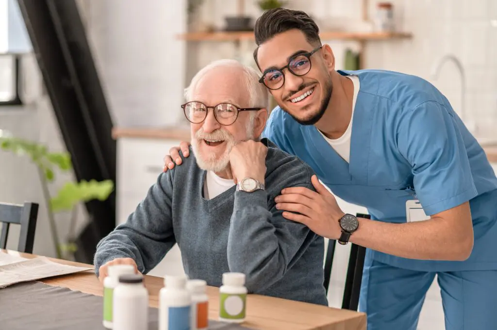 Elderly man and caregiver smiling together indoors.