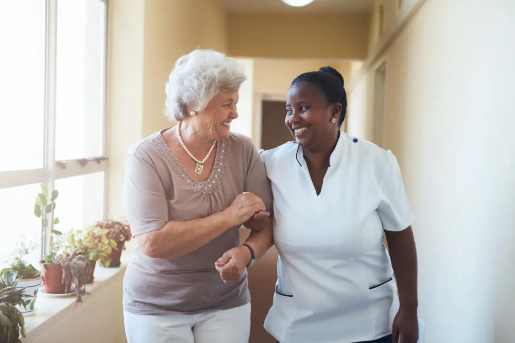 Elderly woman walking with caregiver, smiling.