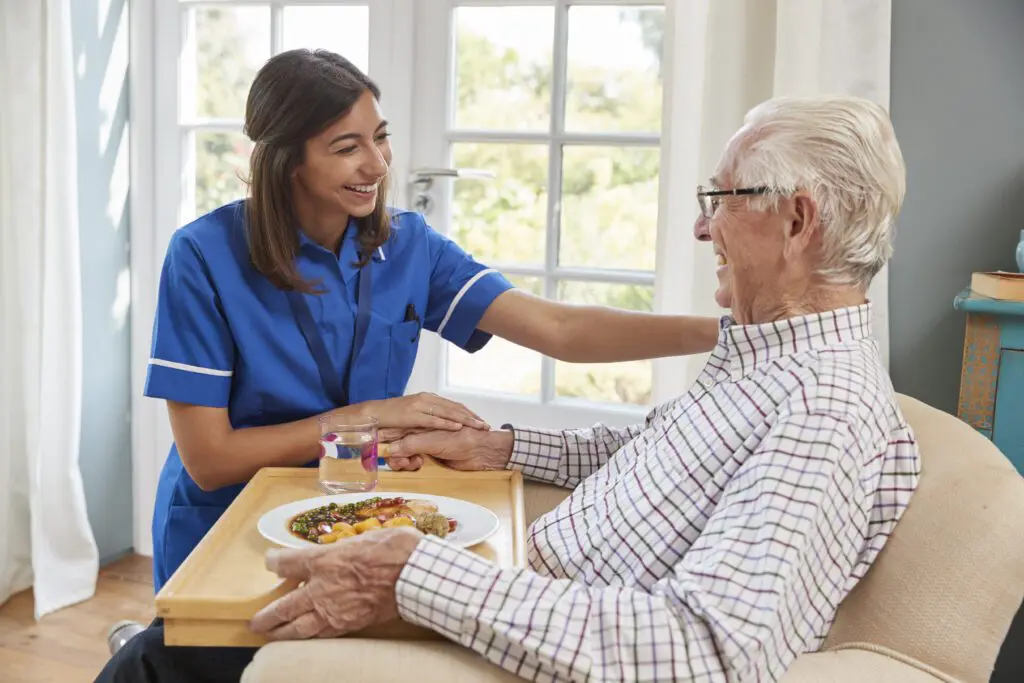 Caregiver smiling with elderly man at home.